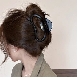 Matte black claw clip with gold French lettering in a stylish hairstyle display
