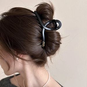 Detail of a large matte black hair claw clip with golden lettering on a French twist hairstyle