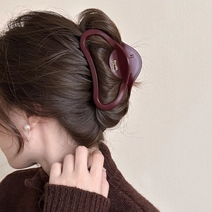 Detail of matte dark red hair claw clip with golden lettering on wavy brown hair