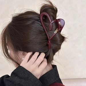 Detail of burgundy heart-shaped hair claw clip with gold script lettering on a bun