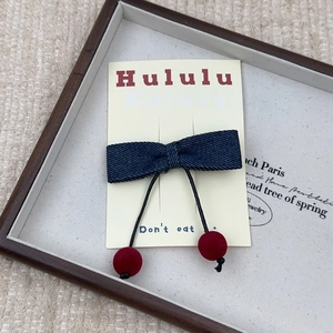 Détail d'un nœud papillon en jean avec cerises en peluche rouges sur plateau en bois