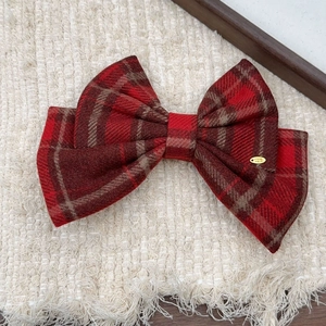 Detail of red plaid bow hair clip with 'Hand Made' gold tag on warm textured background