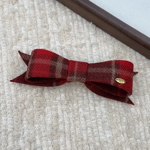 Macro detail of red plaid bow hair clip with handmade metal tag on a knitted background