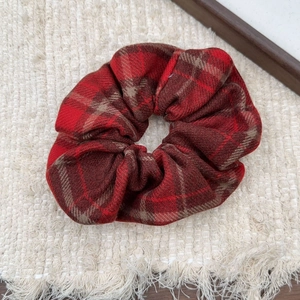 Classic red plaid bow hair scrunchie made of textured cotton fabric on a woven mat