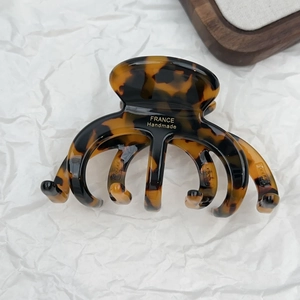 Detail of tortoiseshell hair claw clip with gold France Handmade logo on white textured background