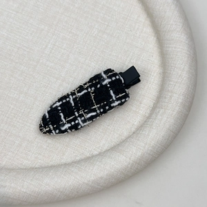 Nahaufnahme der schwarz-weißen Tweed-Haarspange mit goldener Metallseide Details