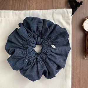 Chouchou en denim bleu foncé avec coutures blanches et logo en argent sur fond en tissu