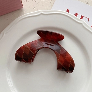 Detailed close-up of retro red plaid claw clip with gold accents on white ceramic plate