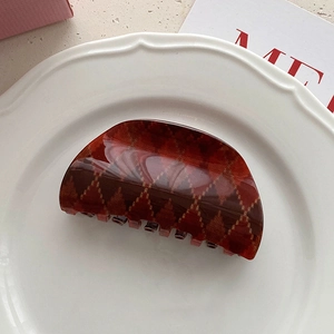 Detail view of red argyle hair claw clip with vintage resin finish on ceramic plate