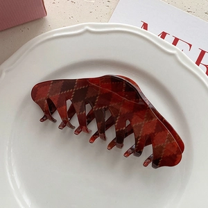 Macro view of dark red plaid hair claw clip on a white ceramic plate for thick hair