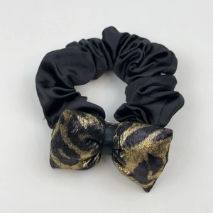 Detail of a black satin scrunchie paired with a golden leopard print bow hair accessory