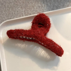 Detail of red plush shark hair clip with silver glitter threads on a white tray