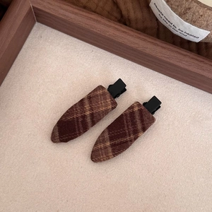 Close-up of brown plaid fabric hair clips with black metal duckbill clips on wood