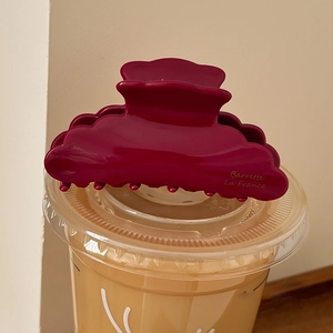 Elegant deep red acetate shark hair claw clip with wavy edges on a clear cup