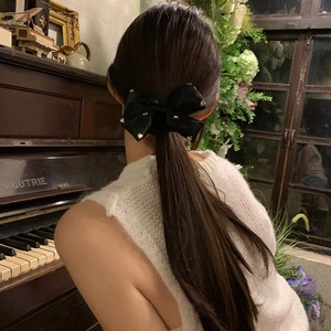 Elegant black satin bow hairclip with sparkling rhinestones worn on a woman's hair