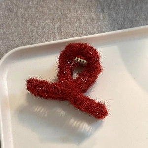 Close-up of a red plush hair claw clip featuring silver glitter silk and golden metal spring