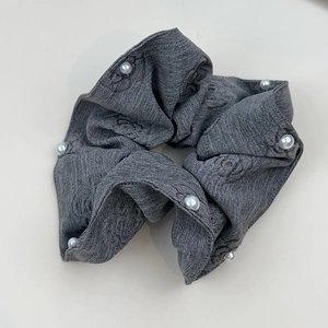 Close-up of charcoal grey fabric scrunchie with camellia pattern and white pearl accents