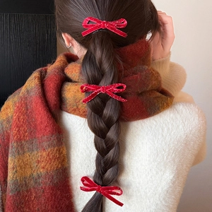 Détail de barrettes nœuds en velours rouge avec paillettes sur une coiffure tressée