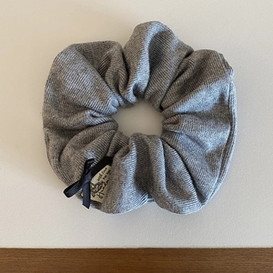 Detail of grey ribbed knit scrunchie with a black satin bow and a sewn-in script label