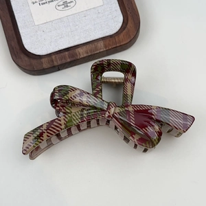 Close-up of a bow-shaped hair claw clip with a red and green tartan plaid pattern texture