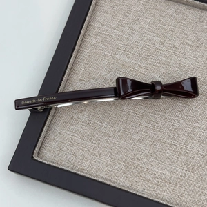 Elegant deep red acetate bow hair clip with gold lettering on a wooden tray