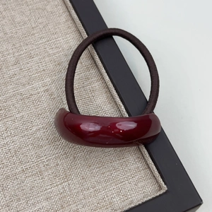 Macro view of high-gloss burgundy resin curved hair tie decoration and woven elastic band