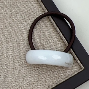 Macro shot of minimalist brown hair tie with white resin arc and Sanshine lettering