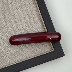 Detailaufnahme einer dunkelroten Acetat-Haarklammer mit Goldaufdruck und Hochglanz-Finish
