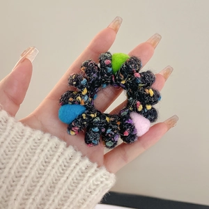 Detail of a black speckled knit scrunchie with colorful plush balls held by hand
