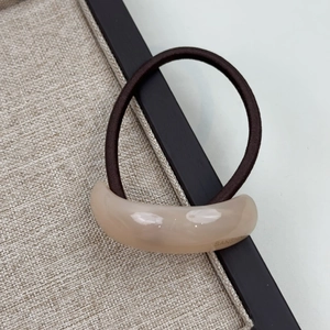 Close-up of a beige resin curved detail with gold lettering on a brown elastic hair tie