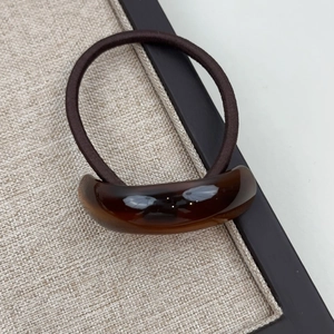 Macro detail of the dark brown high-elastic hair tie with a smooth curved resin buckle