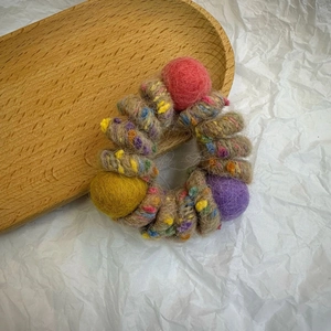 Detail of colorful felt ball telephone wire hair tie with braided woolen fiber texture