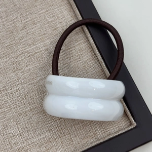 Close-up of white curved resin hair tie with gold label detail on linen tray
