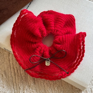Detail of red knitted scrunchie with bow knot and engraved golden metal pendant