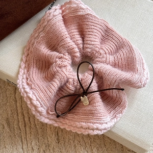 Detail of pink knitted scrunchie with brown bow tie and metallic charm accessory