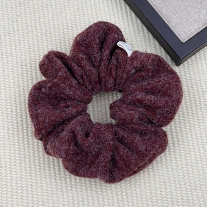 Close-up of deep red plush velvet scrunchie with soft sheepskin texture and logo tag