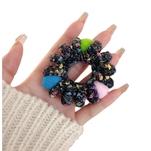 Colorful tweed hair scrunchie with plush pom-poms held by hand on white background