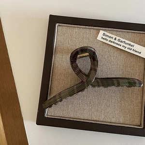 Dettaglio di una pinza per capelli vintage a quadri verdi con molla dorata su legno