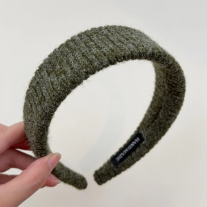 Detailed close-up of dark green knitted headband with thick texture and handmade label