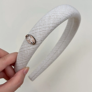 Detailed macro view of cream-colored herringbone fabric headband with bow emblem logo