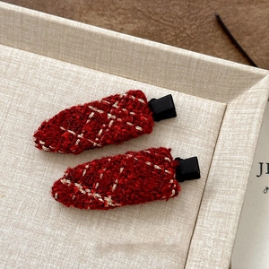 Detailed close-up of red tweed hair clips with gold thread and black duckbill base