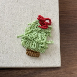 Close-up of a handmade knitted Christmas tree hair clip with a red bow and green yarn texture