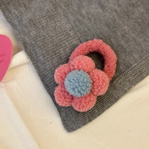 Élastique à cheveux fleur en peluche rose et bleu posé sur un tissu gris texturé