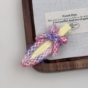 Détail d'une pince à cheveux nœud en tweed rose avec texture tissée sur socle en bois