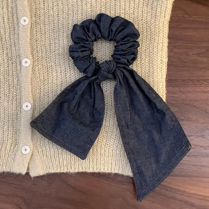 Detail of dark blue denim scrunchie with long ribbon tie on a knit cardigan background