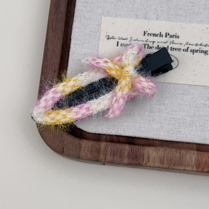 Détail d'une barrette à cheveux en ruban tressé rose et jaune sur plateau en bois