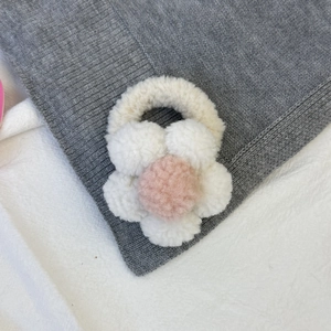 Détail d'un chouchou fleur en peluche crème avec centre rose sur tricot doux