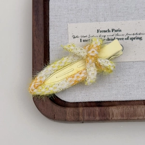 Vue détaillée d'une pince à cheveux en tweed jaune avec fil d'or sur plateau bois