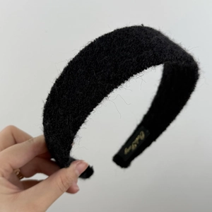 Détail de la texture en peluche noire et de l'étiquette dorée sur le serre-tête large d'hiver