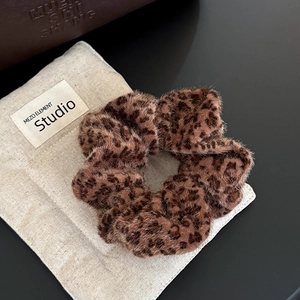 Detail of plush leopard print scrunchie featuring soft texture on rustic beige background